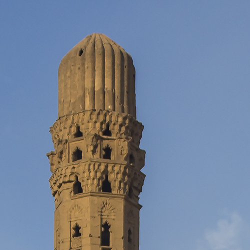 Close-up of an ancient, weathered minaret against a clear blue sky