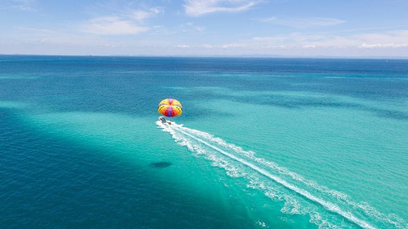 A person parasailing above turquoise waters, towed by a boat on a sunny day.