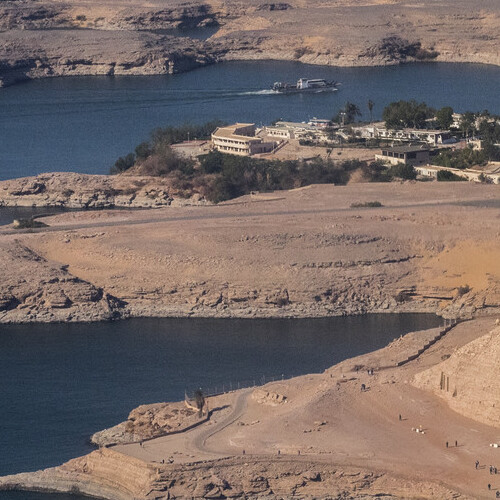 Aerial view of a serene riverside landscape with buildings and boats, surrounded by barren hills.