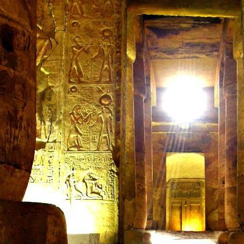 Interior view of an ancient Egyptian temple with hieroglyphs and pillars illuminated by sunlight
