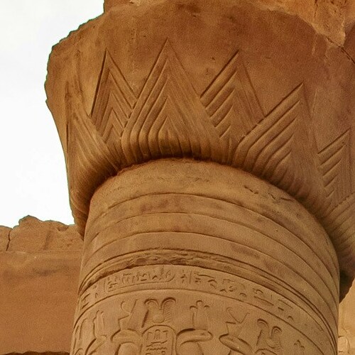Close-up of the top of an ancient column with hieroglyphic carvings and palm-like capital