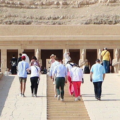 A group of tourists walking towards the entrance of an ancient temple with statues on either side