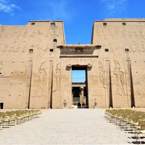 Front view of the Edfu Temple in Egypt, showcasing intricate carvings on massive sandstone walls under a clear blue sky.