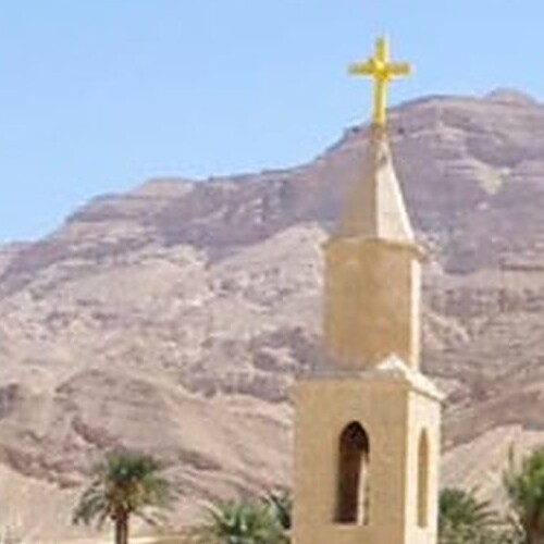 A church spire with a cross on top against the backdrop of arid mountains and a clear sky.