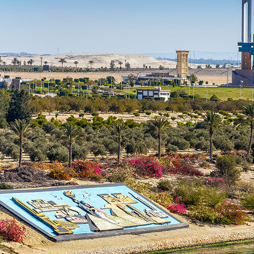 Colorful mosaic art installation in the foreground with a lush green park and desert landscape in the background