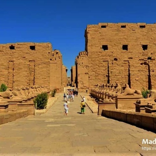 Visitors walking through the towering entrance of Karnak Temple under a clear blue sky