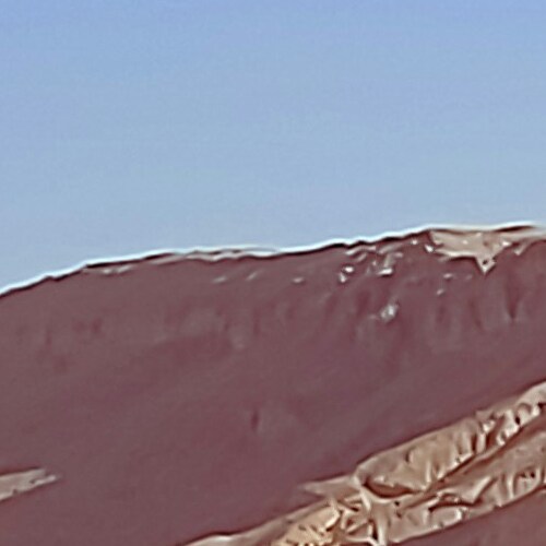 A close-up of a ridged, crimson sand dune under a clear sky