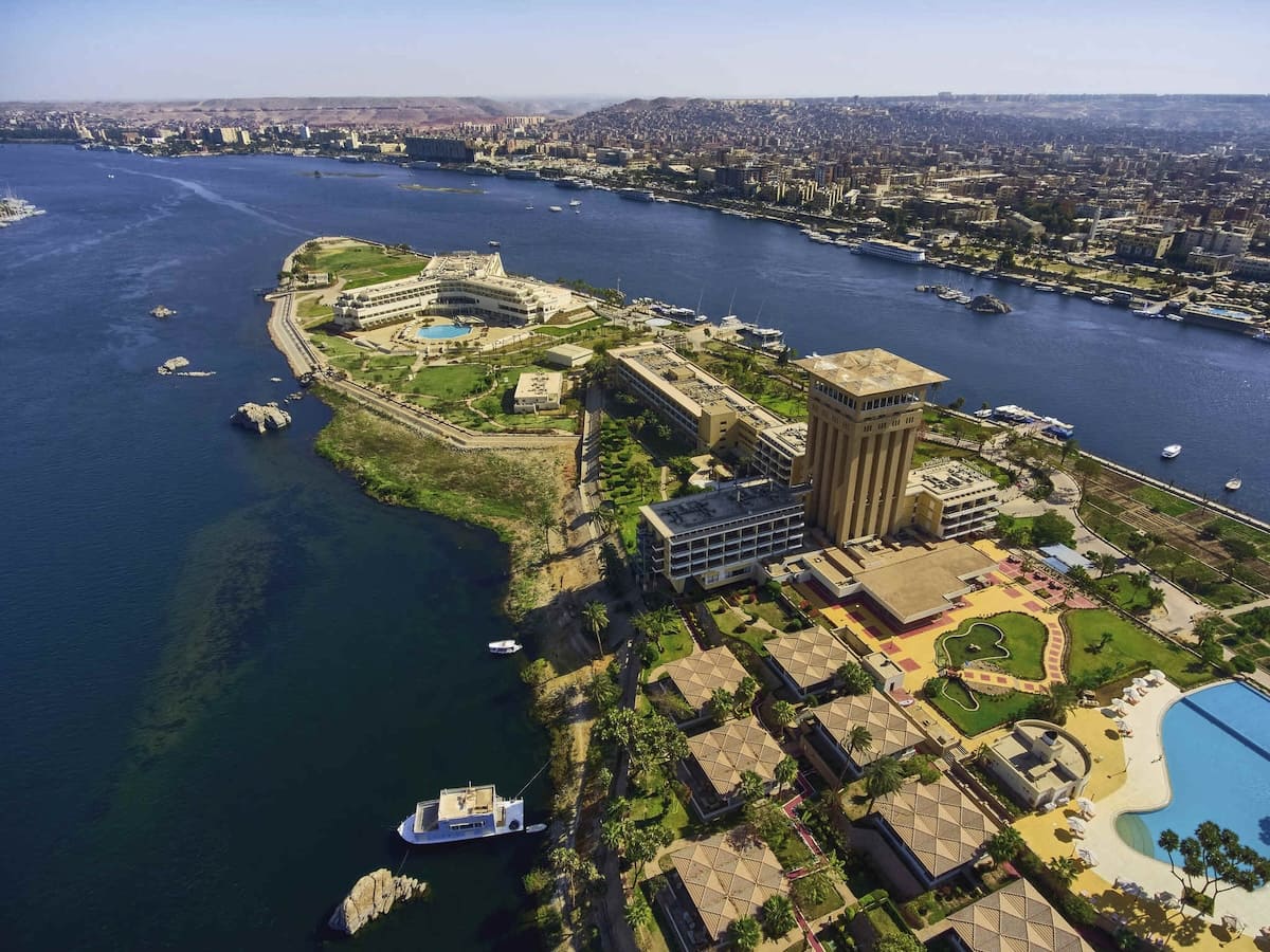 Scenic view of the Mövenpick Aswan Resort, showcasing its lush gardens, luxurious pool area, and striking architecture against a backdrop of the Nile River