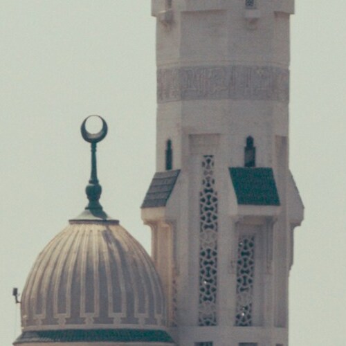 Close-up of a mosque's dome and minaret with a crescent moon symbol at the top against a clear sky