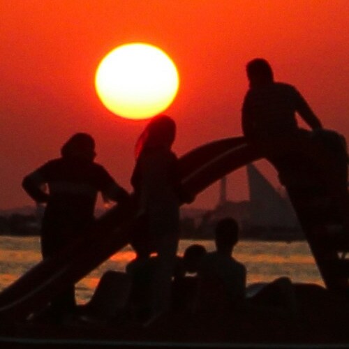 Silhouettes of people playing on a beach structure against a vibrant sunset