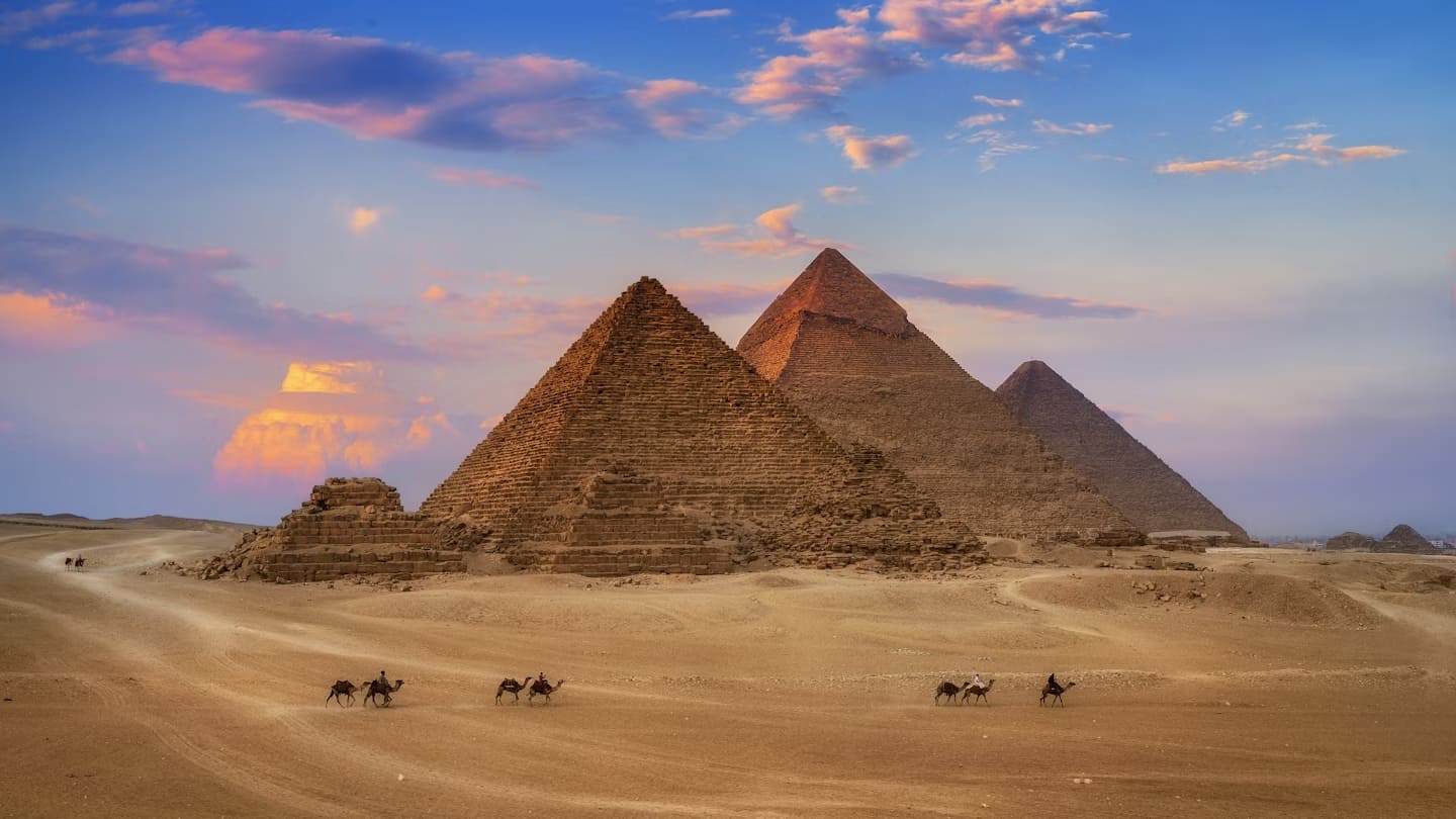 Iconic view of the Pyramids of Giza under a clear blue sky, showcasing the monumental structures and surrounding desert landscape