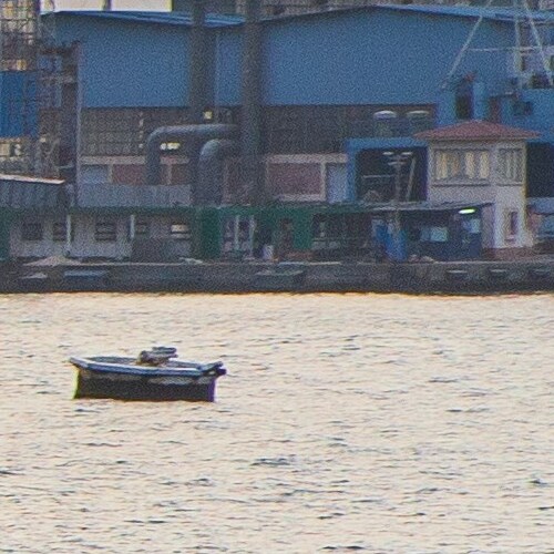 A small boat floating alone on the water with an industrial backdrop