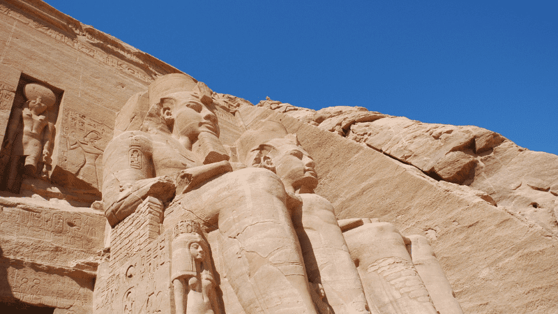 Colossal statues of Pharaoh Ramses II carved into the facade of Abu Simbel temple in Egypt, against a clear blue sky
