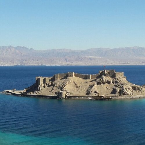 Aerial view of Salah El-Din's castle surrounded by clear blue waters near Taba, with mountains in the background