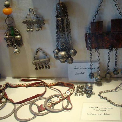 A collection of traditional Siwan jewelry, including silver necklaces and amulets, displayed in a museum case