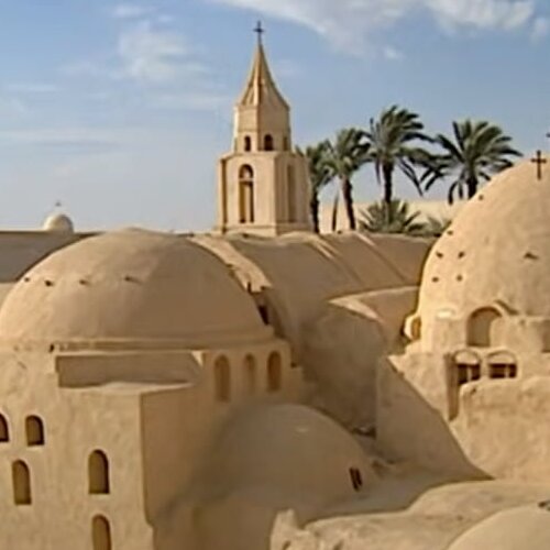 Ancient domed Coptic monasteries with a tall bell tower nestled among palm trees in Wadi El Natron, Egyp