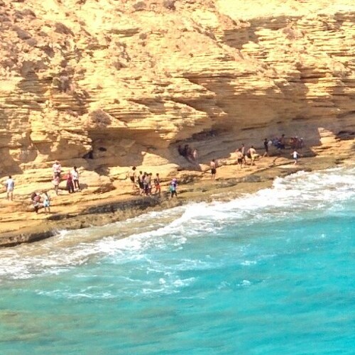 A group of people standing on sedimentary rock layers by the turquoise sea