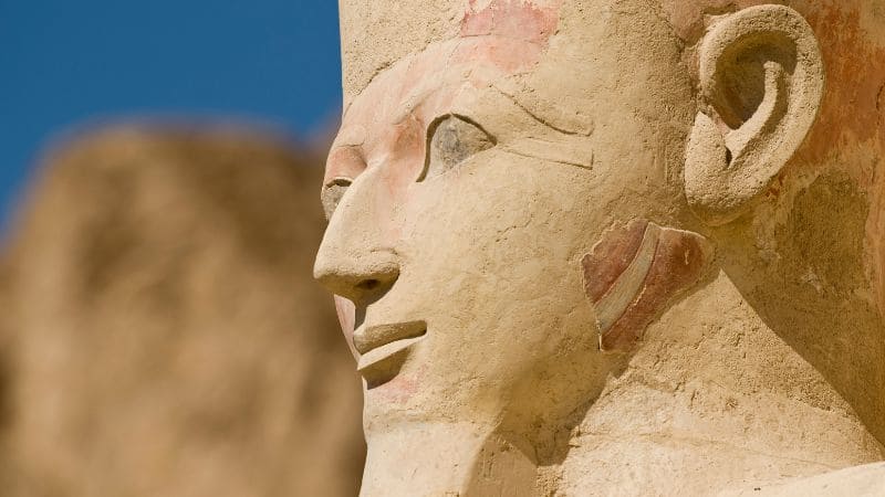Close-up of the face of the Great Sphinx with the Pyramid of Khafre in the background.