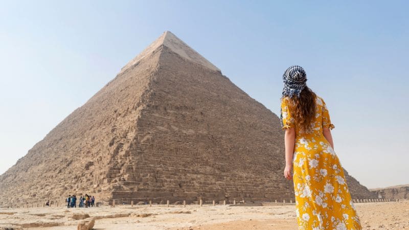 A woman in a floral dress looking up at the Pyramid of Khufu in Giza.