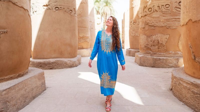 Woman in blue traditional dress walking between the columns of an Egyptian temple