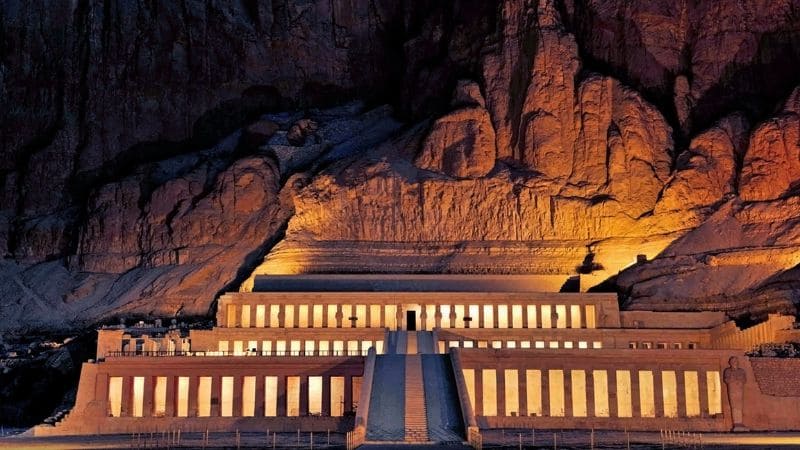Night view of a lit-up temple complex against rocky mountains in Egypt.