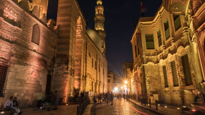 Historic buildings and a mosque in the evening lights on an old Cairo street.