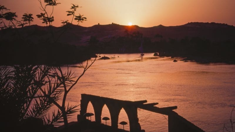 Sunset view over the Nile with silhouettes of palm trees and ruins in Aswan.