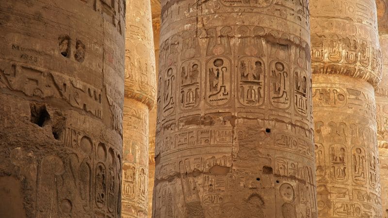 Sunlit columns with hieroglyphs inside an Egyptian temple.