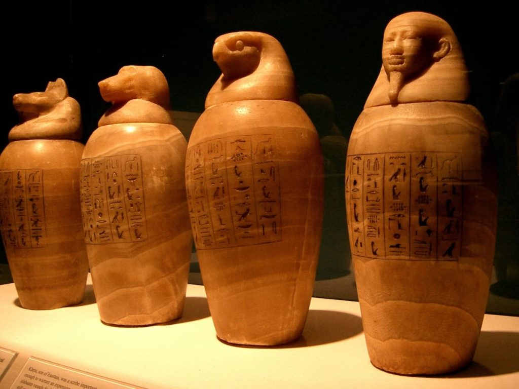 Four ancient Egyptian canopic jars displayed in a museum, featuring hieroglyphics and human-shaped lids.