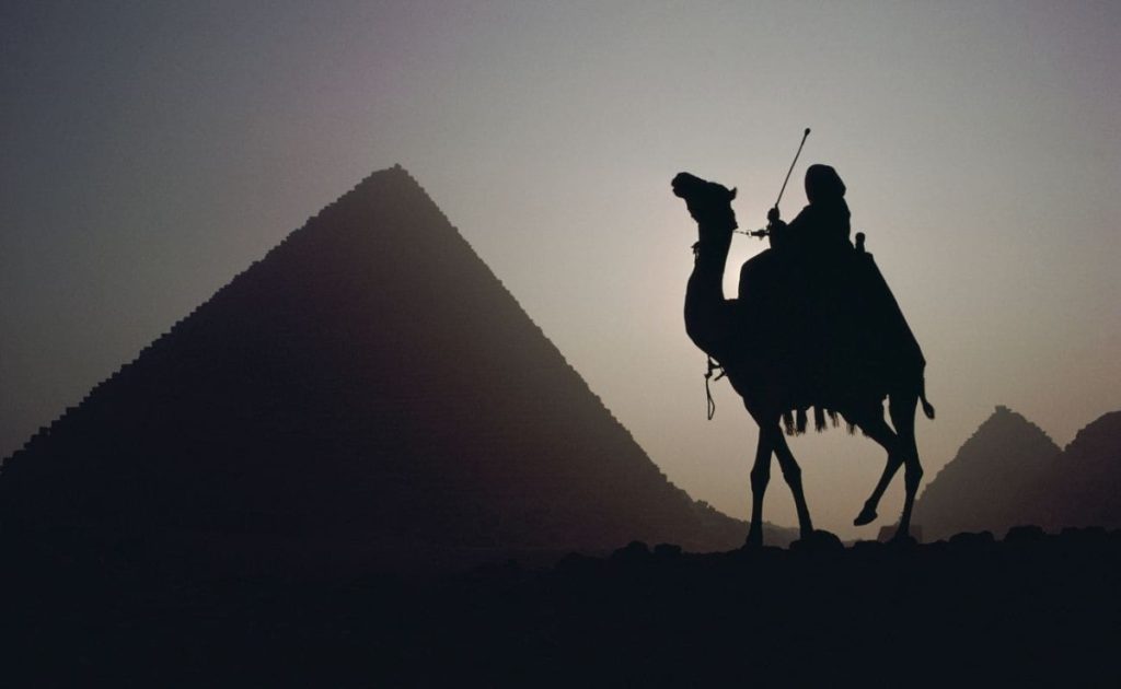 Camel rider silhouetted against the backdrop of the Pyramids of Giza at sunset.