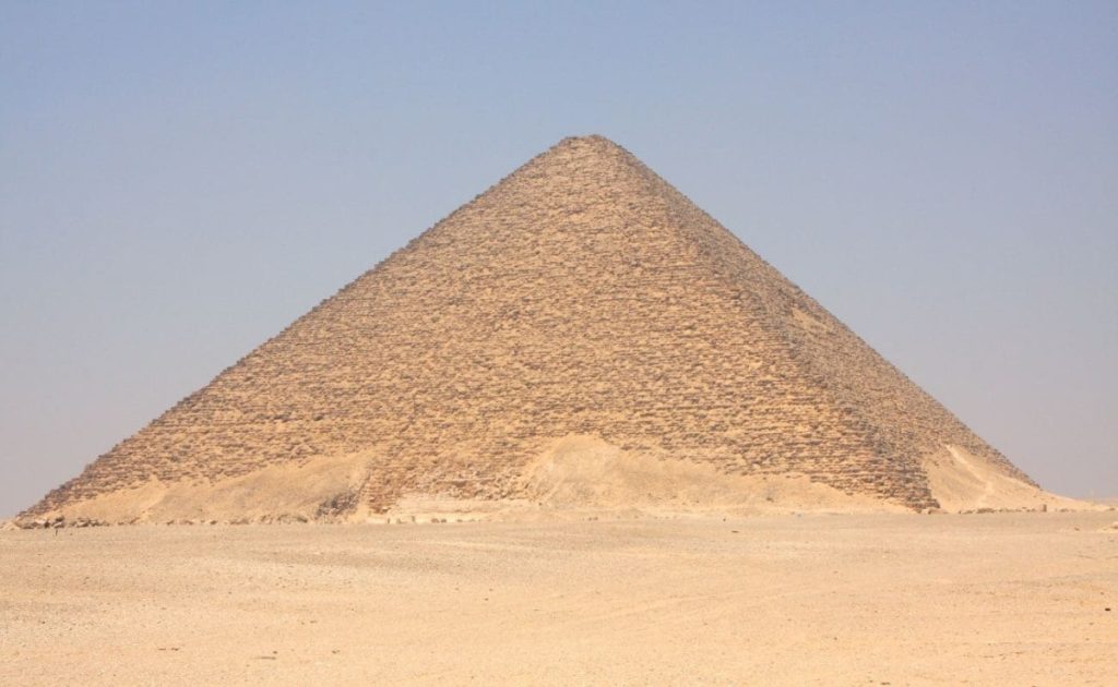 The Red Pyramid at Dahshur, standing isolated against a clear blue sky on a vast desert landscape.