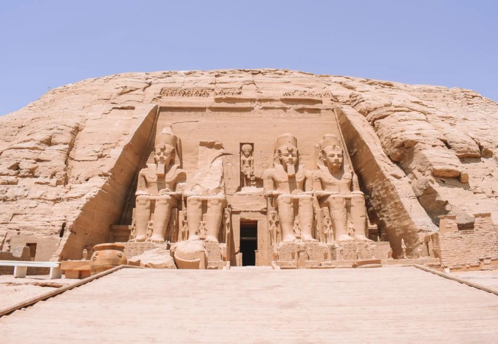 The twin temples of Abu Simbel with their colossal statues of Pharaoh Ramses II, bathed in sunlight, overlooking a clear blue sky