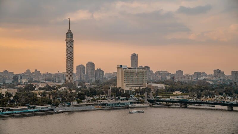 Sunset view over Cairo featuring the iconic Cairo Tower and the Nile River, with cityscape and boats in the foreground