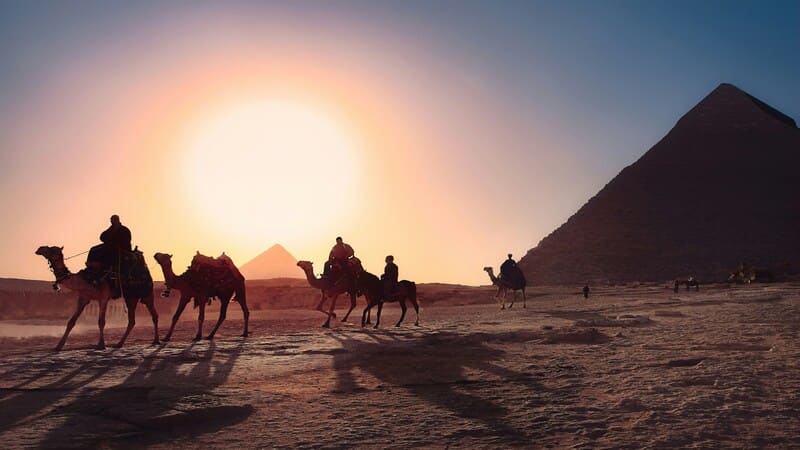 Silhouettes of camels and riders against the backdrop of the Great Pyramid at sunset in Giza, Egypt