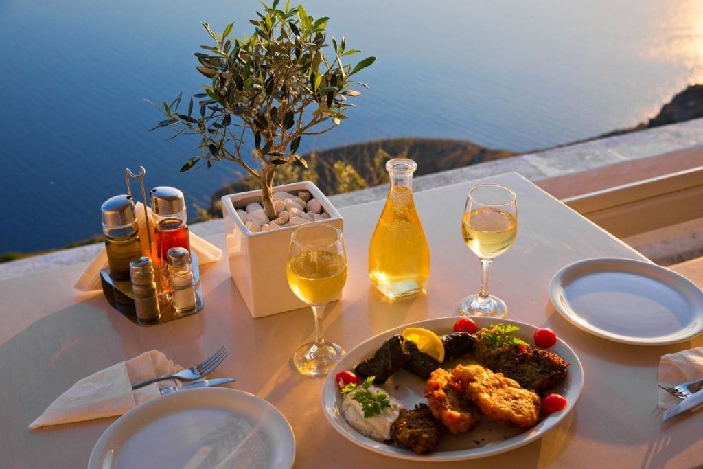 A cliffside table set with a meal and wine, overlooking the vast sea during sunset