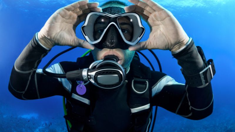 A scuba diver gives the OK signal, framed by deep blue ocean waters