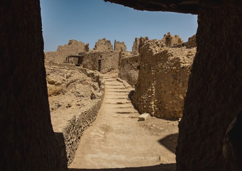 View through an ancient stone archway revealing the ruins of Siwa Oracle Temple under a clear blue sky