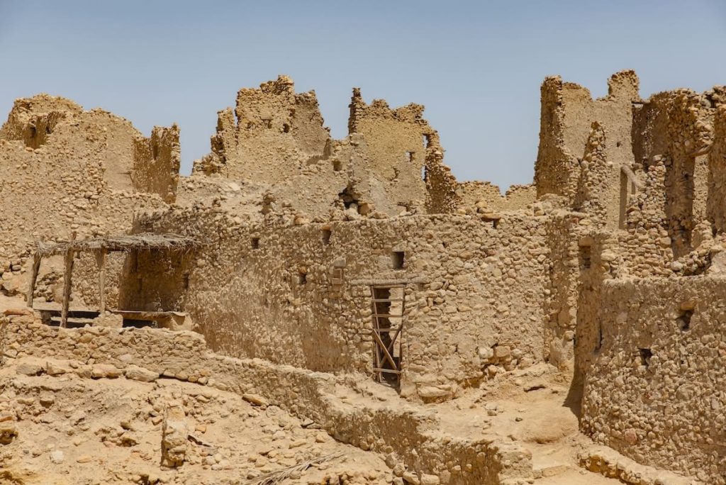 The ancient Temple of the Oracle in Siwa Oasis, Egypt, featuring weathered stone ruins set against a clear blue sky and the stark desert landscape