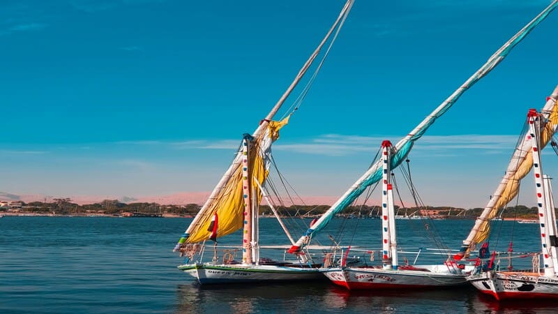 Colorful feluccas with bright sails moored on the blue waters of the Nile River under a clear sky