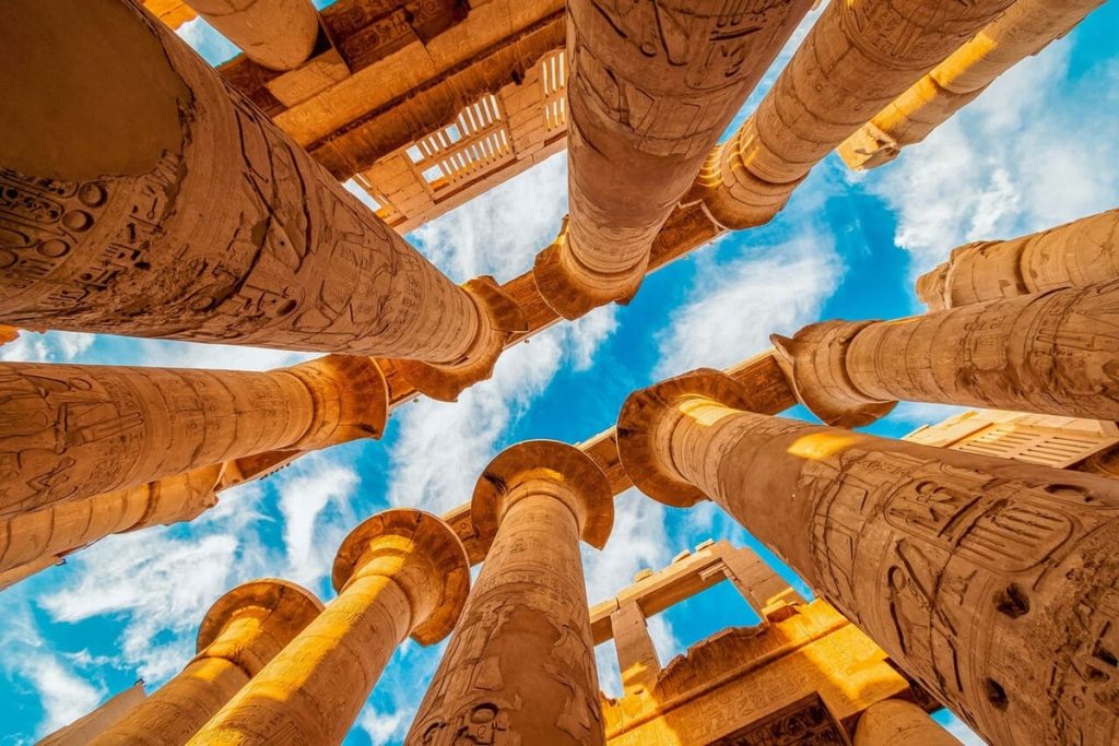 View from below of towering columns at Luxor Temple, featuring intricate hieroglyphics against a clear blue sky.