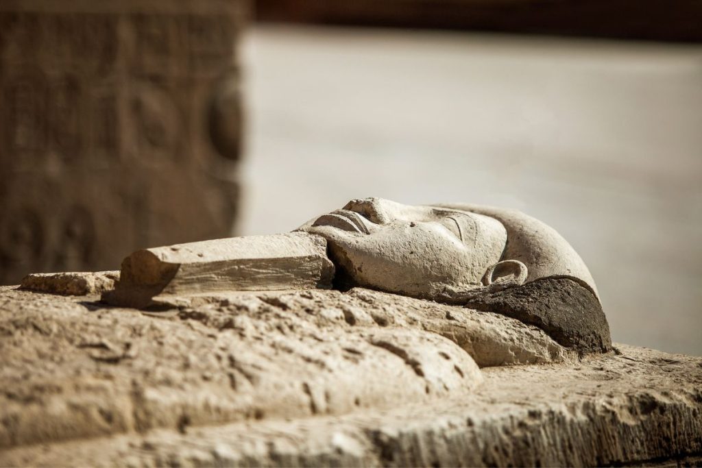 Close-up of a fallen pharaoh statue's head lying on the ground, symbolising the enduring legacy of Egypt's ancient rulers