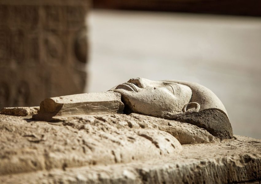 Close-up of a fallen pharaoh statue's head lying on the ground, symbolising the enduring legacy of Egypt's ancient rulers