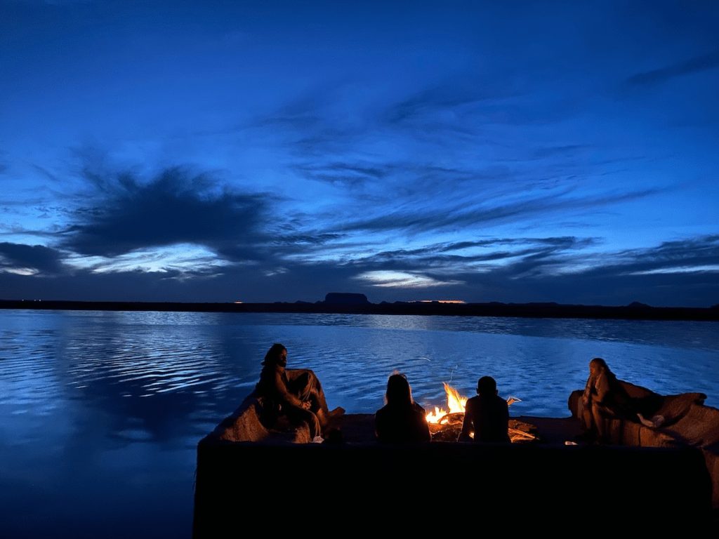 Group of friends enjoying a campfire by a lakeside under a twilight sky.