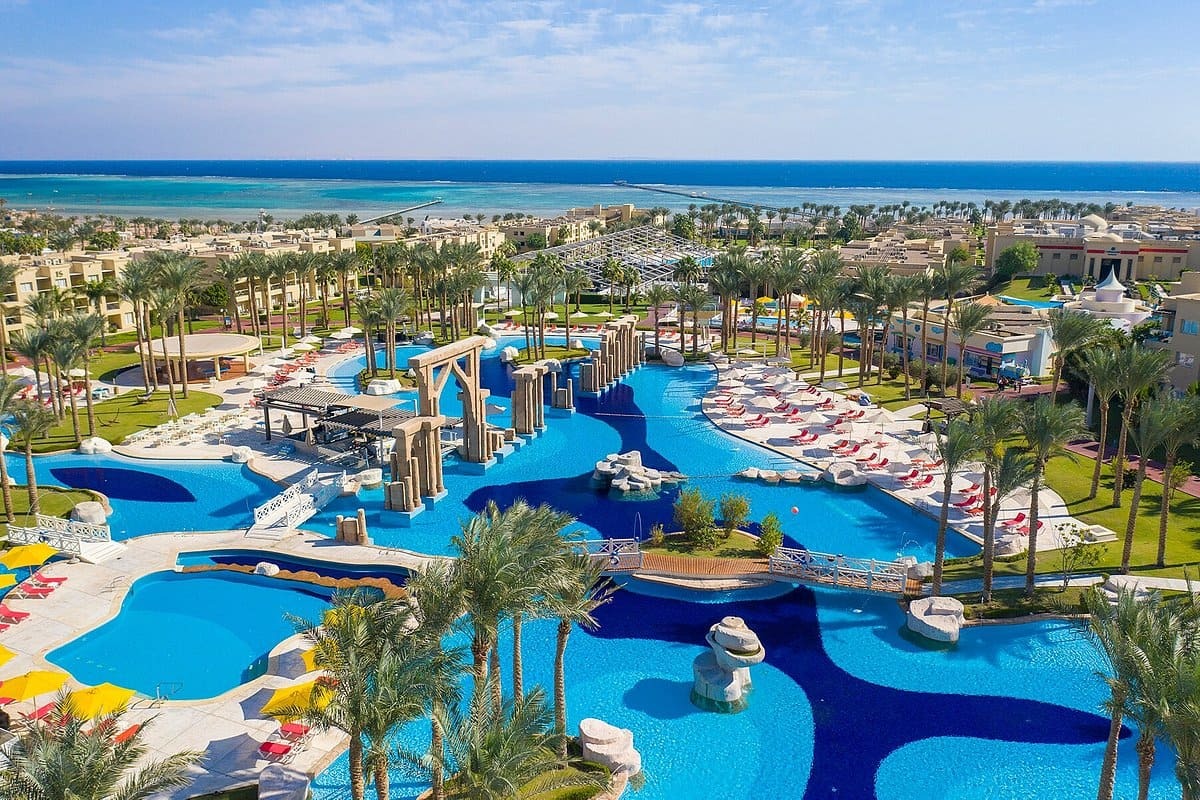 Aerial view of a sprawling resort with multiple swimming pools, sun loungers, and a view of the sea in Egypt
