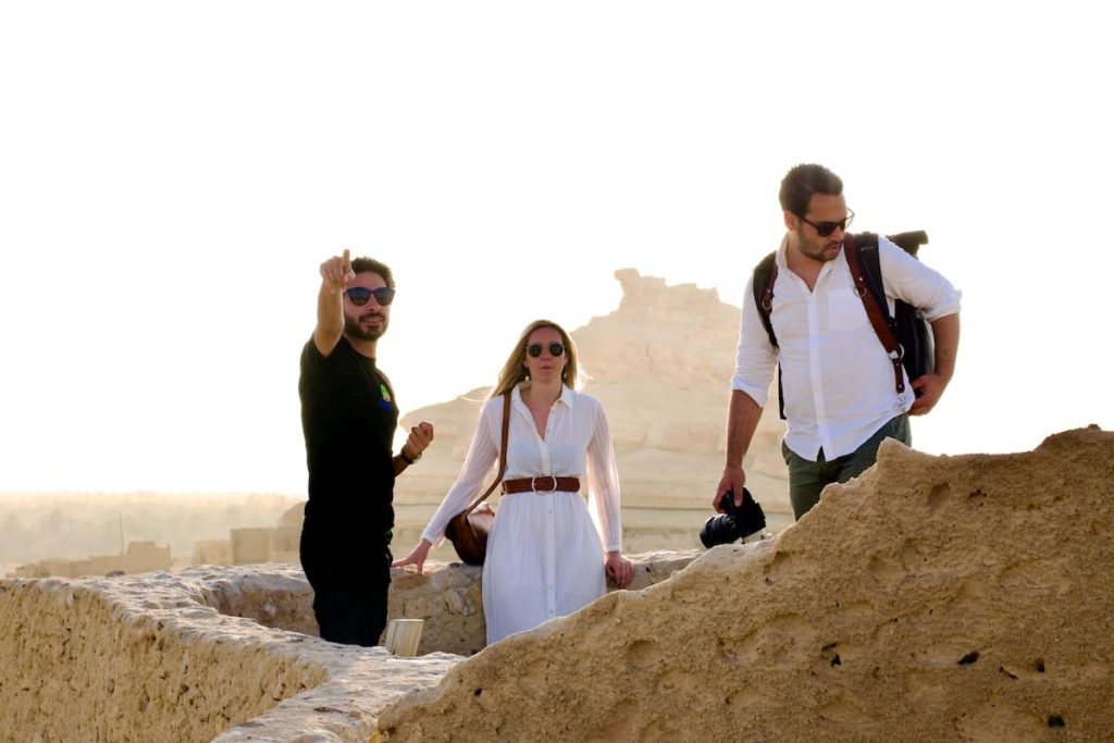 Three travelers exploring an ancient Egyptian fortress, with one pointing into the distance, highlighting historical landmarks in the arid landscape