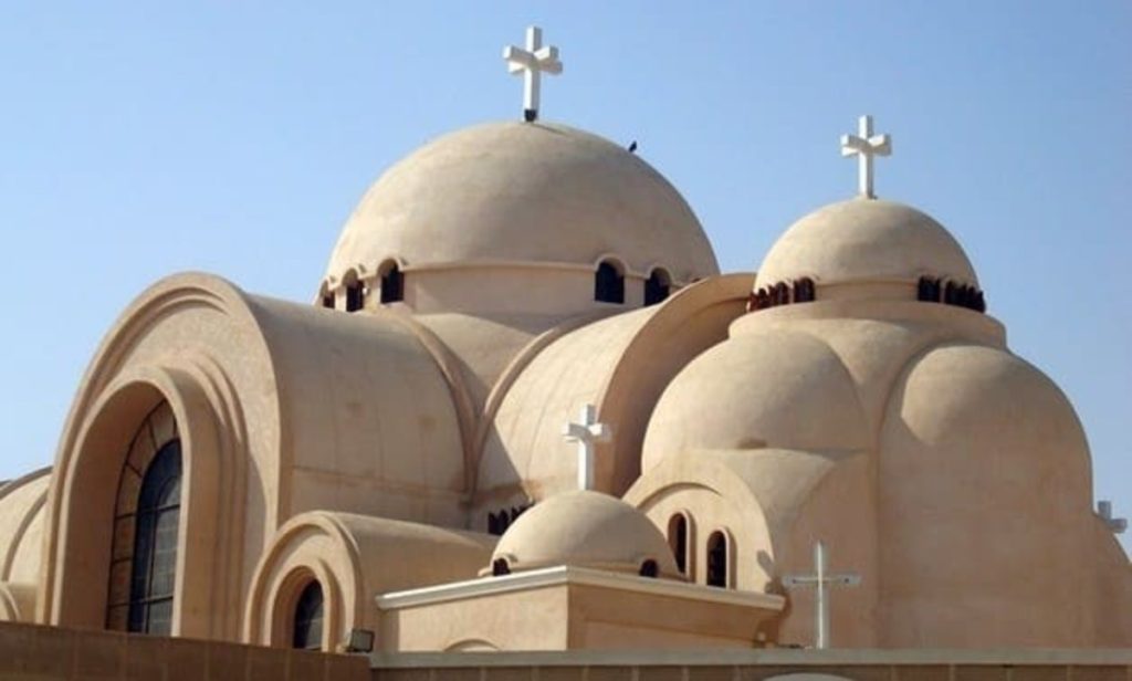 A view of a modern Coptic church featuring multiple domes adorned with crosses against a clear sky.