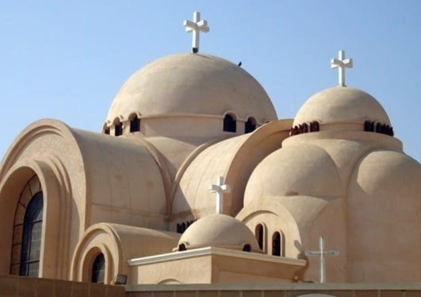 A view of a modern Coptic church featuring multiple domes adorned with crosses against a clear sky.