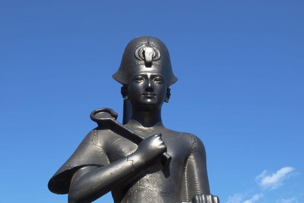 A photo of a majestic black statue of Pharaoh Ramses II set against a clear blue sky