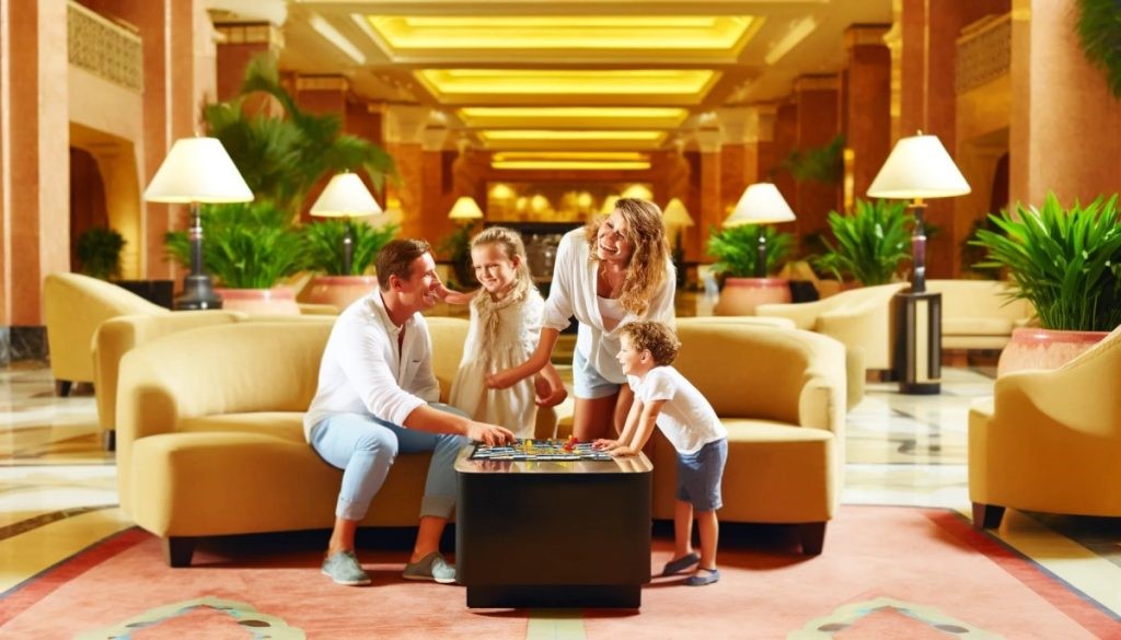 A family of four enjoying a game in the opulent lobby of a luxurious hotel, surrounded by lush green plants and elegant furnishings