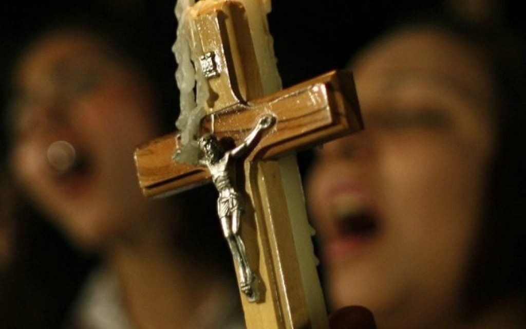 Close-up of a wooden cross with a silver figure of Jesus, held by a blurred figure in the background, symbolizing deep spiritual devotion.